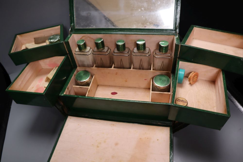 A 1930s ladies green leather travelling toilet case, fittings include seven glass and enamelled bottles, 32cm, in original travelling